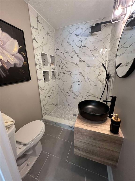 bathroom with a tile shower, tile patterned flooring, vanity, and toilet