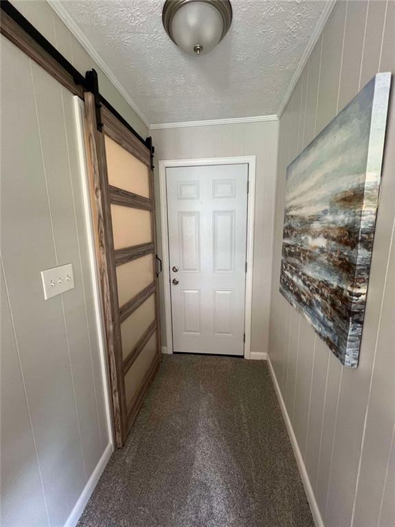 doorway featuring carpet flooring, a textured ceiling, crown molding, and a barn door