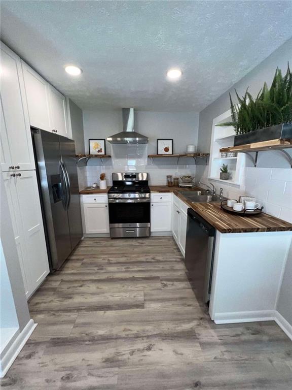 kitchen featuring white cabinets, sink, wall chimney exhaust hood, light hardwood / wood-style flooring, and appliances with stainless steel finishes