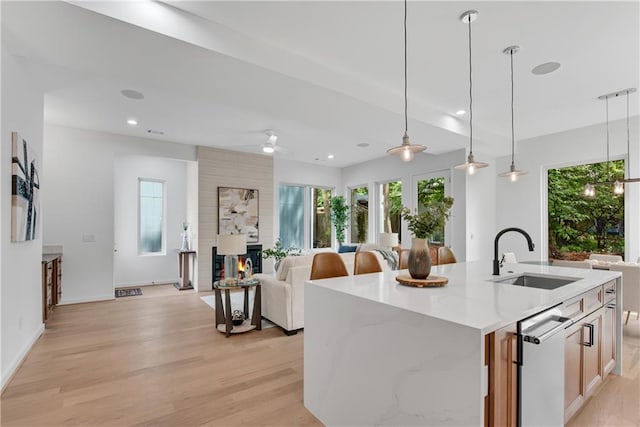 kitchen featuring ceiling fan, sink, hanging light fixtures, light hardwood / wood-style floors, and a kitchen island with sink