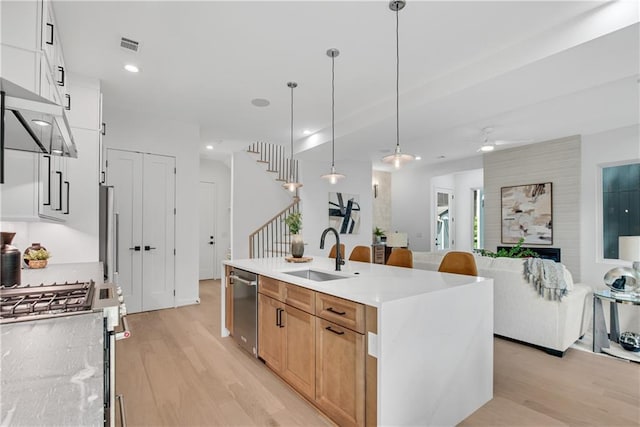 kitchen with a kitchen island with sink, sink, appliances with stainless steel finishes, decorative light fixtures, and white cabinetry