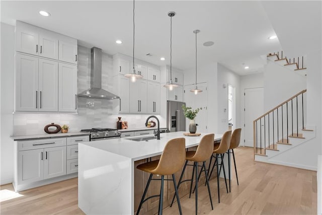 kitchen with appliances with stainless steel finishes, sink, wall chimney range hood, pendant lighting, and a center island with sink