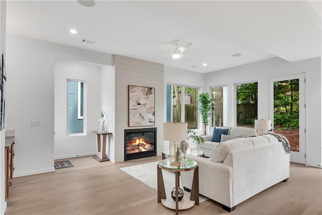 living room featuring a large fireplace, light hardwood / wood-style flooring, and ceiling fan