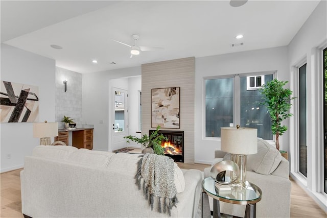 living room featuring ceiling fan, a large fireplace, and light hardwood / wood-style flooring