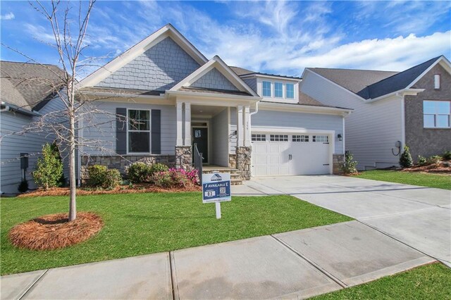 craftsman-style home featuring stone siding, a front lawn, a garage, and concrete driveway