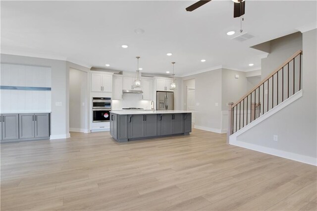 kitchen with stainless steel appliances, a center island with sink, light wood-type flooring, light countertops, and under cabinet range hood