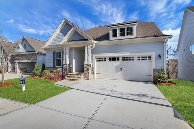 craftsman house with stone siding, an attached garage, driveway, and a front yard