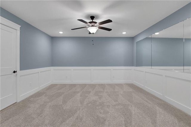 empty room with recessed lighting, a ceiling fan, a decorative wall, wainscoting, and light colored carpet