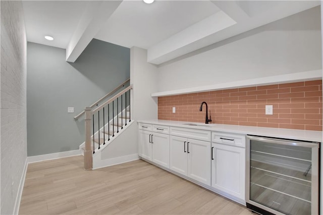 bar featuring wine cooler, a sink, baseboards, light wood-style floors, and decorative backsplash