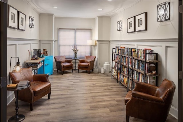 living area featuring a decorative wall, crown molding, and wood finished floors