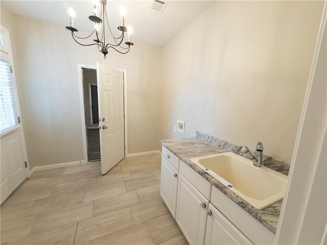 kitchen featuring light stone countertops, sink, pendant lighting, an inviting chandelier, and white cabinetry