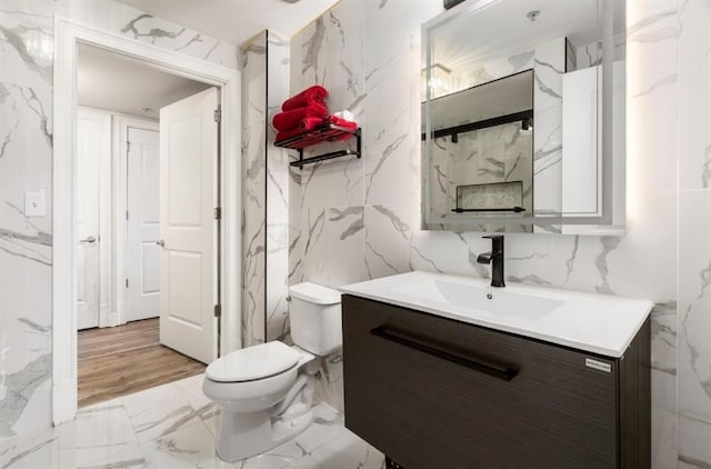 bathroom with vanity, stone wall, toilet, and marble finish floor