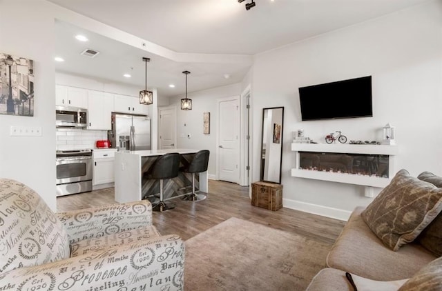 living area with visible vents, baseboards, recessed lighting, a glass covered fireplace, and light wood-type flooring