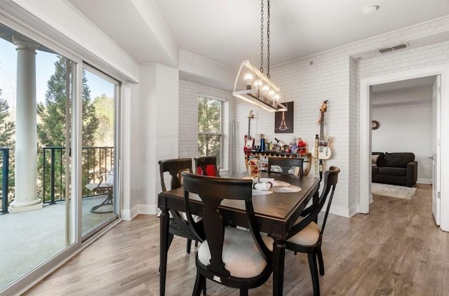 dining area featuring visible vents, light wood-style flooring, brick wall, and baseboards