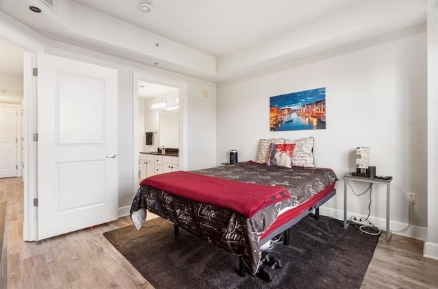 bedroom with ensuite bathroom, baseboards, and light wood finished floors