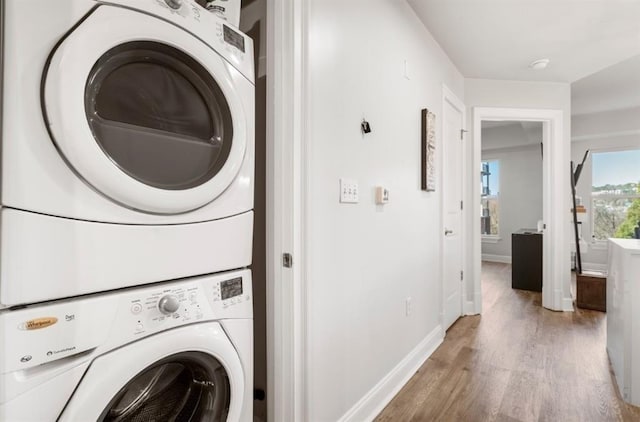 laundry room with baseboards, light wood finished floors, laundry area, and stacked washer / dryer