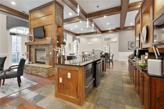 kitchen featuring dark countertops, stainless steel microwave, beamed ceiling, stone tile floors, and a stone fireplace