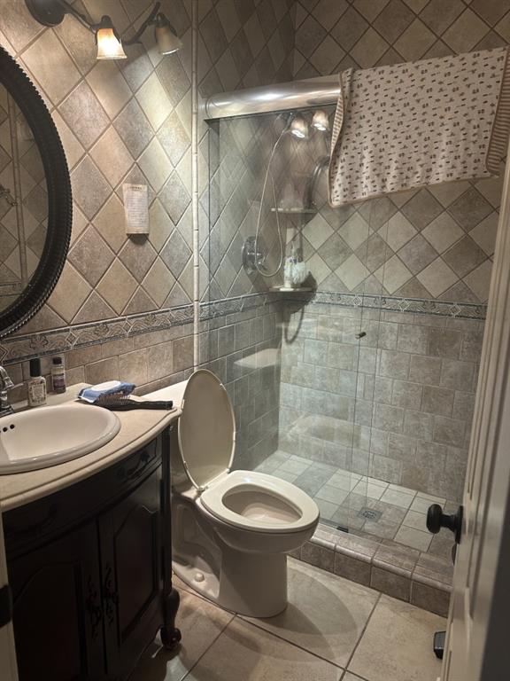 bathroom featuring vanity, a shower with door, tile patterned floors, toilet, and tile walls