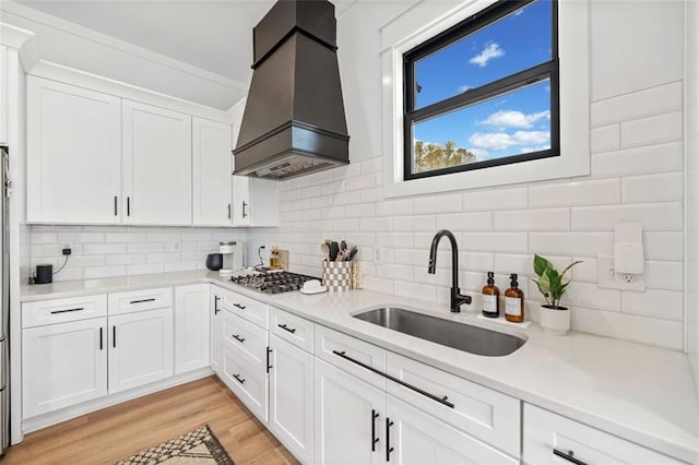 kitchen featuring a sink, light wood-style floors, light countertops, custom exhaust hood, and stainless steel gas stovetop