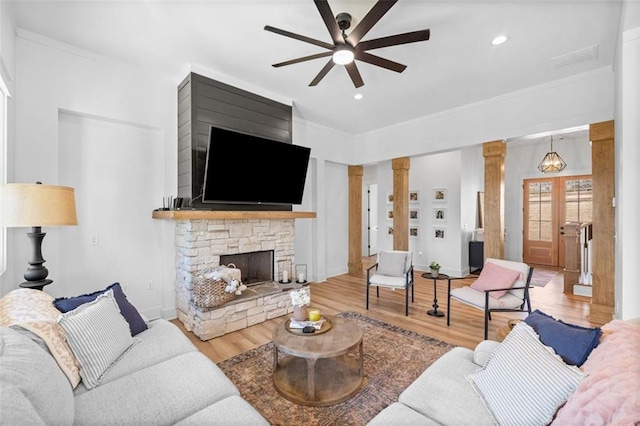 living area featuring decorative columns, ornamental molding, wood finished floors, and a stone fireplace