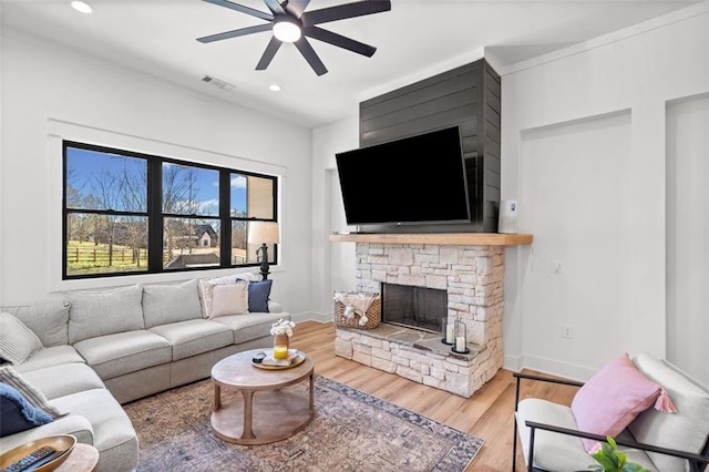 living room featuring baseboards, visible vents, wood finished floors, and a stone fireplace