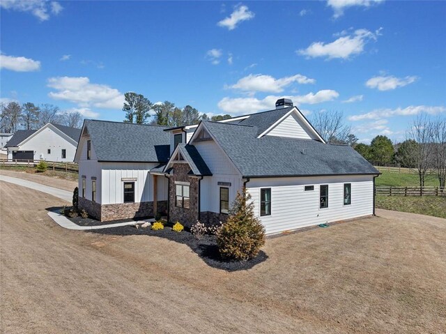 view of front of home featuring board and batten siding, stone siding, fence, and a shingled roof