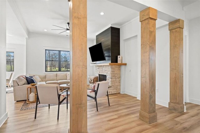 living area with light wood-style floors, decorative columns, a ceiling fan, and a stone fireplace