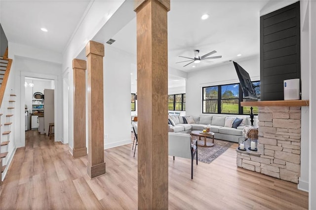 living area featuring light wood-type flooring, ornate columns, ceiling fan, and visible vents