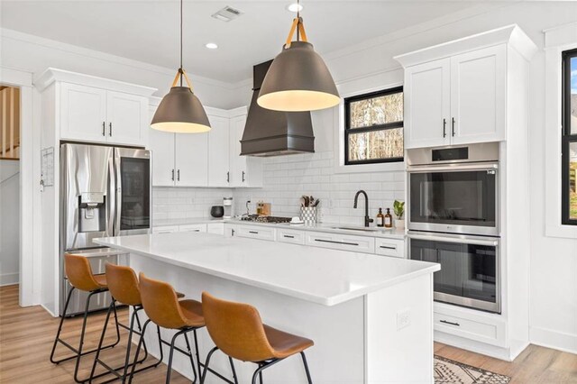 kitchen featuring custom exhaust hood, stainless steel appliances, light countertops, a kitchen bar, and a sink