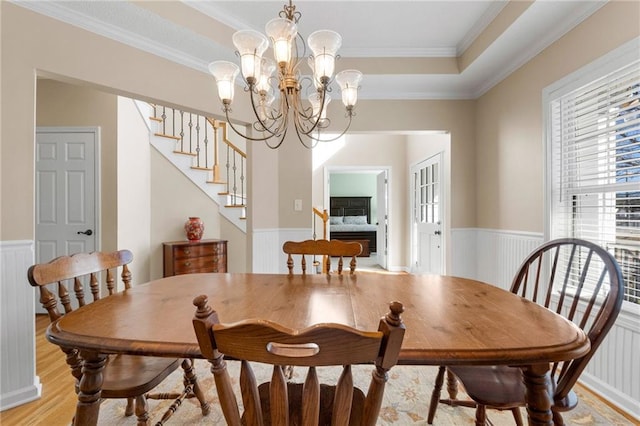 dining area with a raised ceiling, an inviting chandelier, ornamental molding, and light hardwood / wood-style floors