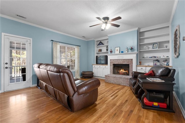 living room featuring built in features, a brick fireplace, crown molding, and a textured ceiling