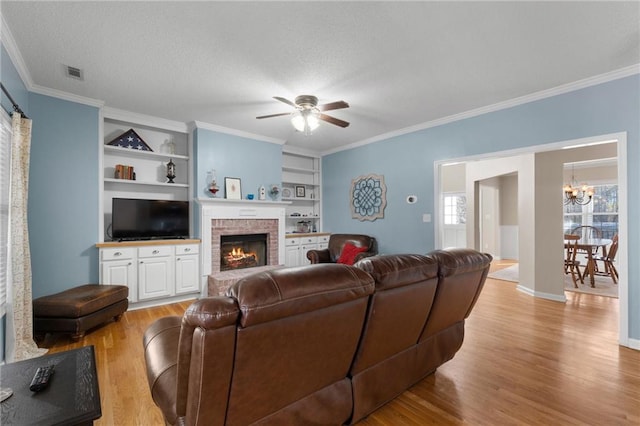 living room with a brick fireplace, light hardwood / wood-style floors, built in features, a textured ceiling, and ceiling fan with notable chandelier