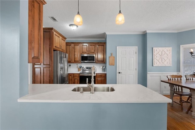 kitchen featuring pendant lighting, appliances with stainless steel finishes, sink, kitchen peninsula, and crown molding