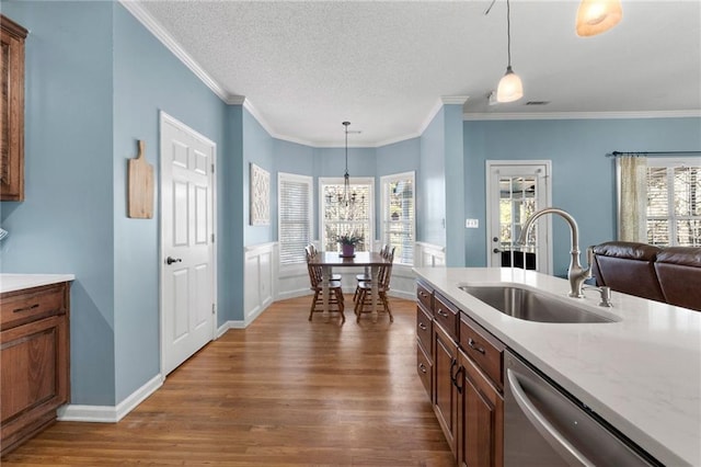 kitchen with stainless steel dishwasher, sink, crown molding, and pendant lighting