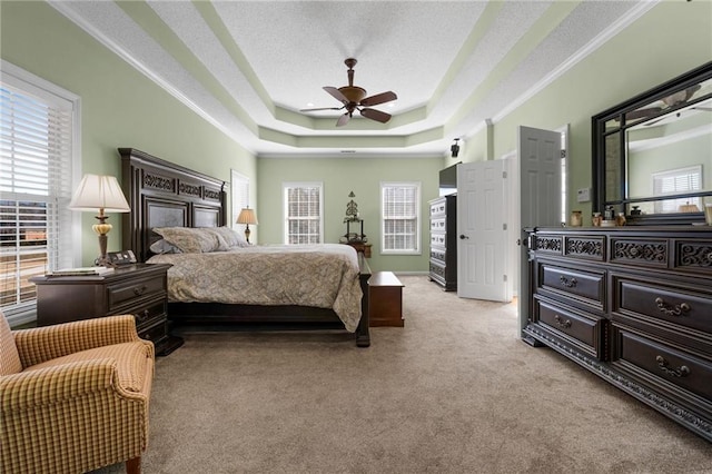 carpeted bedroom with ceiling fan, a tray ceiling, a textured ceiling, and ornamental molding