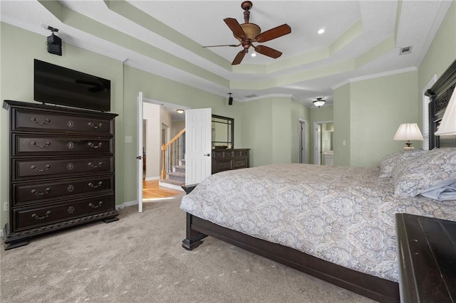 bedroom featuring ensuite bathroom, ceiling fan, a tray ceiling, light colored carpet, and crown molding