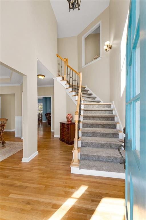 staircase featuring a towering ceiling, crown molding, and hardwood / wood-style flooring