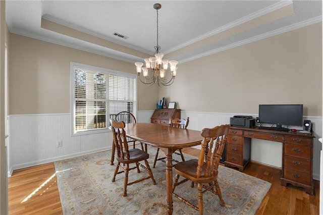 dining room with a raised ceiling, a notable chandelier, ornamental molding, and dark wood-type flooring