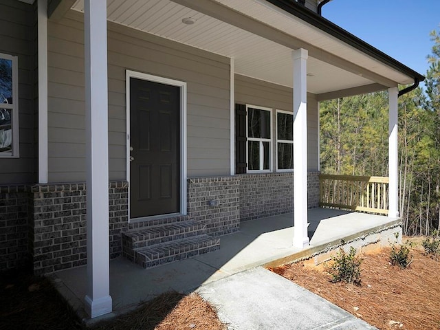 view of exterior entry with a porch and brick siding