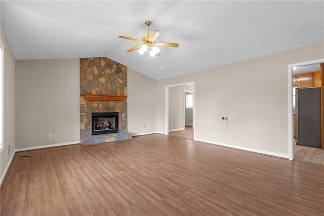 unfurnished living room featuring hardwood / wood-style flooring, ceiling fan, a stone fireplace, and vaulted ceiling