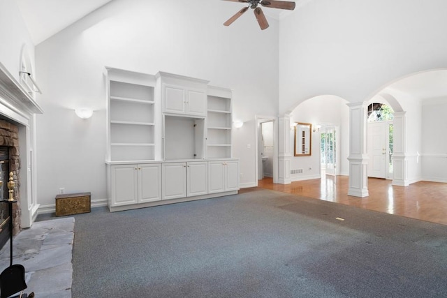 unfurnished living room featuring wood-type flooring, a fireplace, decorative columns, ceiling fan, and high vaulted ceiling