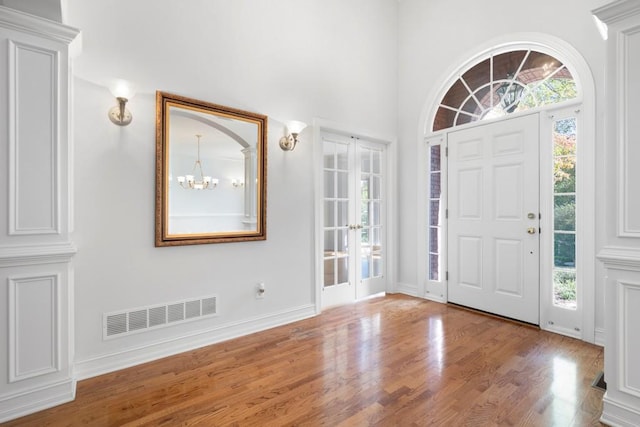 entrance foyer with a towering ceiling, light hardwood / wood-style flooring, ornate columns, and an inviting chandelier