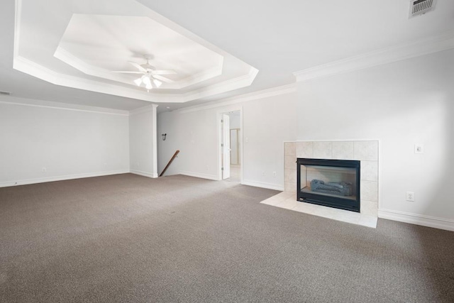 unfurnished living room featuring a raised ceiling, a tiled fireplace, ceiling fan, crown molding, and light colored carpet