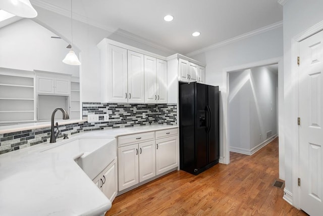 kitchen featuring black fridge, white cabinetry, pendant lighting, light hardwood / wood-style floors, and crown molding