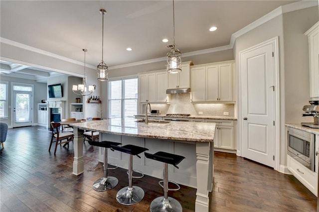 kitchen featuring backsplash, a sink, stainless steel microwave, under cabinet range hood, and recessed lighting