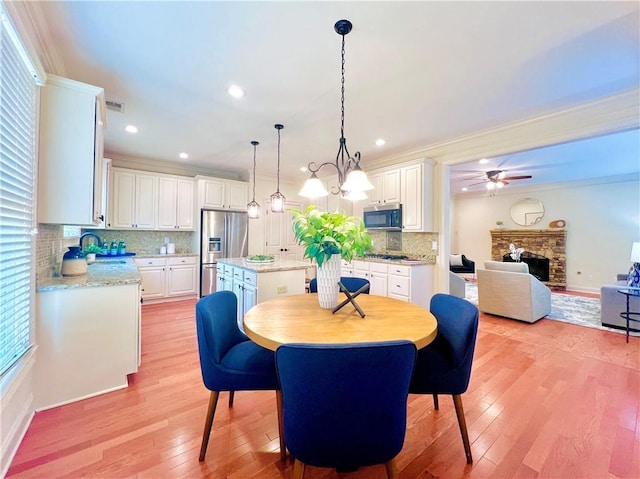 dining room featuring ceiling fan with notable chandelier, a fireplace, sink, ornamental molding, and light wood-type flooring