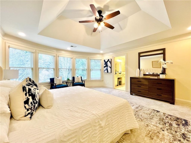 carpeted bedroom featuring a raised ceiling, ceiling fan, ornamental molding, and ensuite bath