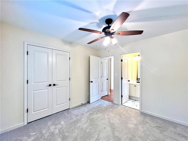 unfurnished bedroom featuring ensuite bathroom, light carpet, ceiling fan, and a closet