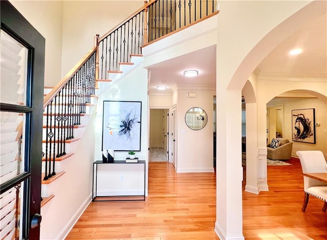 entrance foyer featuring crown molding, a towering ceiling, and light hardwood / wood-style floors