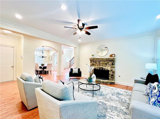 living room featuring crown molding, a fireplace, light hardwood / wood-style floors, and ceiling fan with notable chandelier